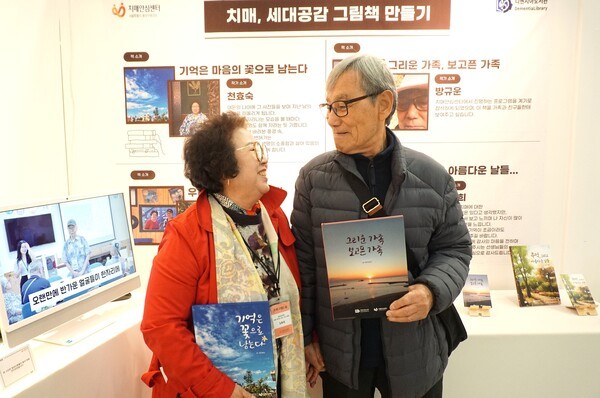 그림책 제작 프로그램에 참여한 노부부가 '치매 안심 케어 로그인(Care Login) 박람회'에서 본인들이 손수 만든 책을 들고 서로를 바라보고 있다. / 디멘시아뉴스